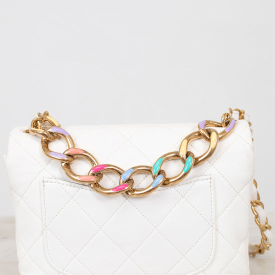 White quilted handbag with a gold chain strap featuring colorful links on a white background