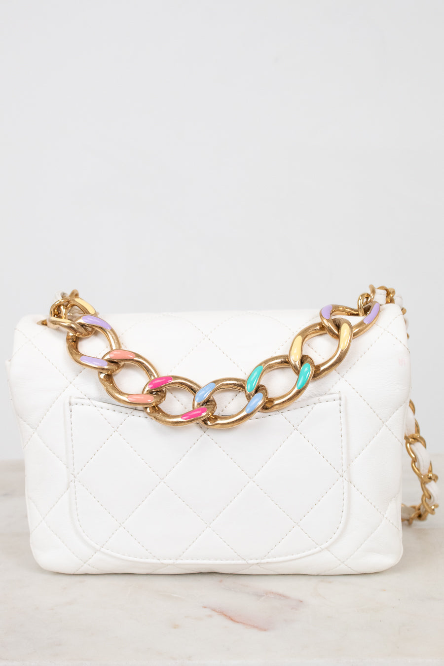 White quilted handbag with a gold chain strap featuring colorful links on a white background