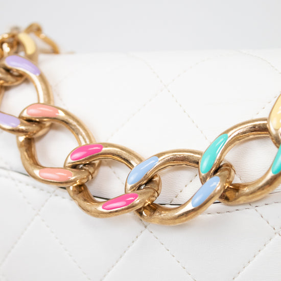 Gold chain bracelet with colorful links on a white quilted surface