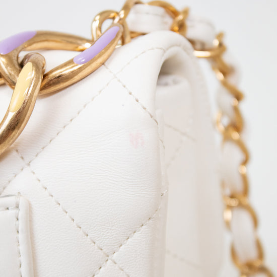 Close-up of a white quilted handbag with gold chain handle on a light gray background