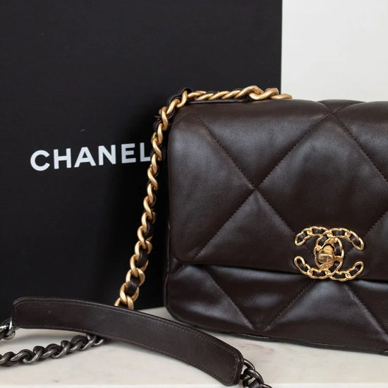 Dark Brown quilted Chanel handbag with gold chain and clasp on a white surface, with a black Chanel box in the background.