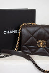 Dark Brown quilted Chanel handbag with gold chain and clasp on a white surface, with a black Chanel box in the background.