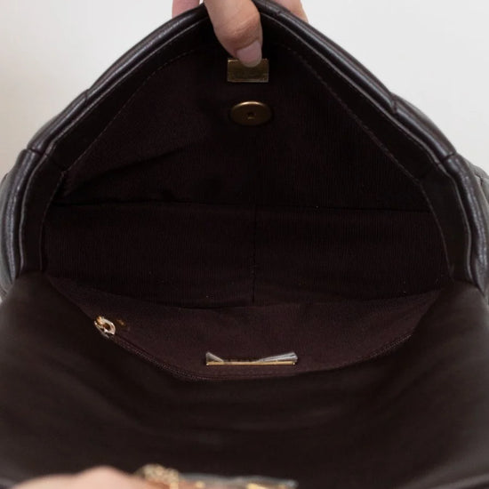 Close-up of a hand holding a dark brown handbag with gold accents.