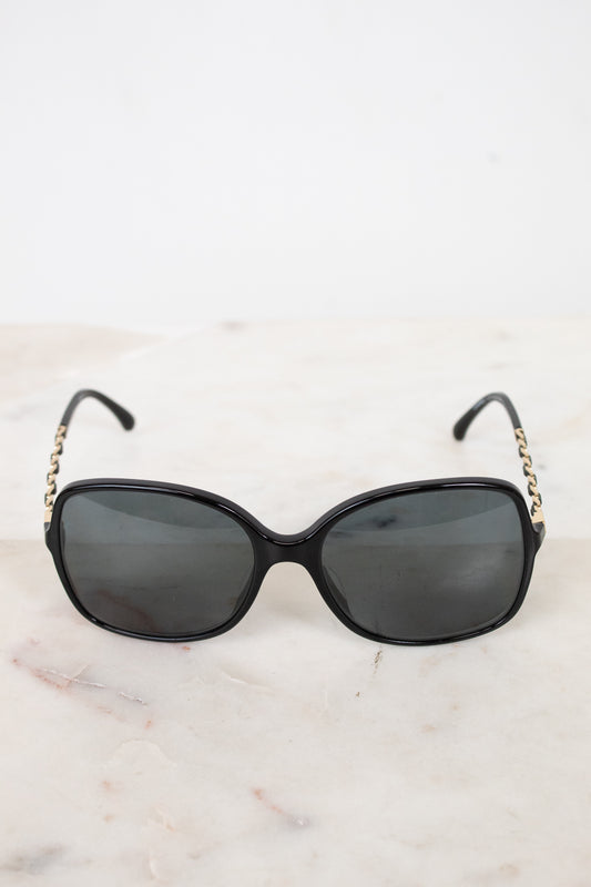 Black sunglasses with gold chains on sides sitting on a marble surface