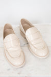 A pair of cream-colored leather loafers with decorative stitching, displayed on a white marble surface against a white background.