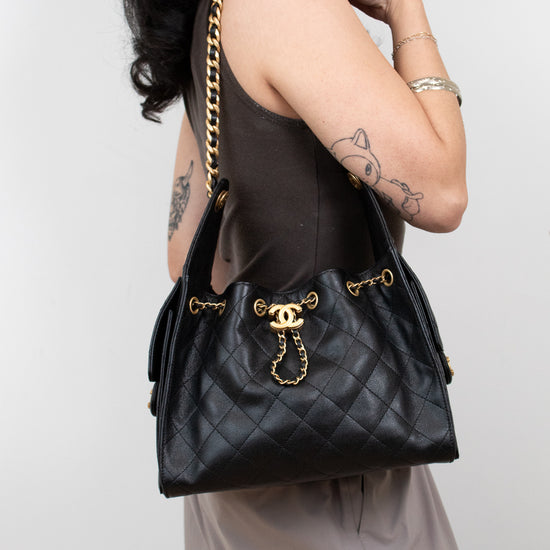Person holding a black quilted handbag with gold hardware against a white background