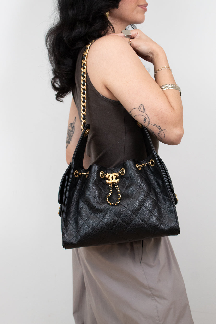 Person holding a black quilted handbag with gold hardware against a white background