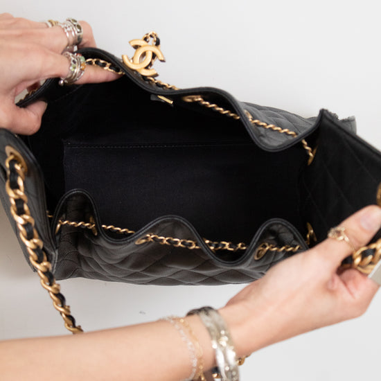 Black handbag with gold chain detail held by a person against a white background