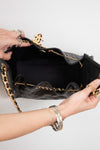 Black handbag with gold chain detail held by a person against a white background