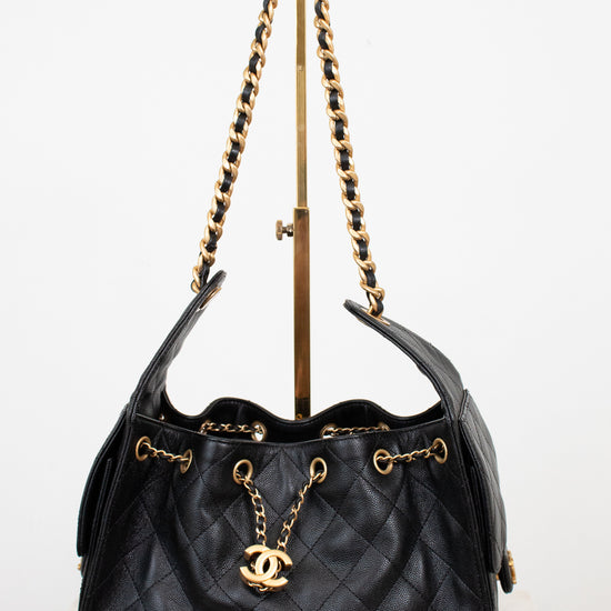 Black quilted handbag with gold chain and logo on a white background