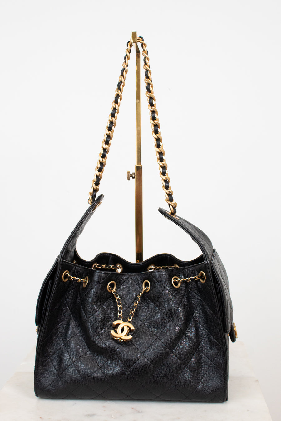 Black quilted handbag with gold chain and logo on a white background
