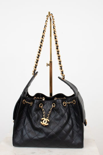 Black quilted handbag with gold chain and logo on a white background
