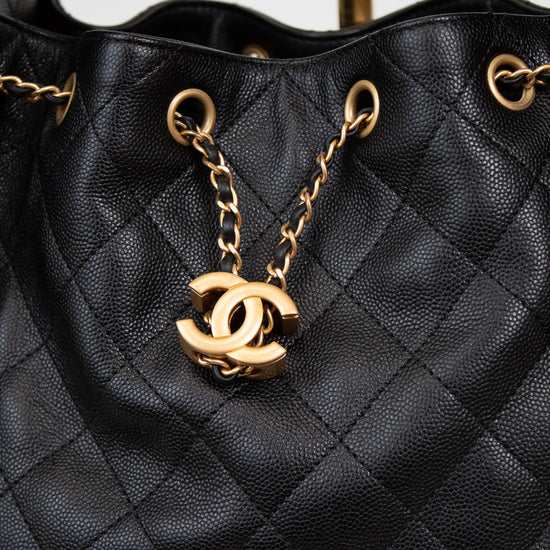Black quilted handbag with gold chain and CC logo on a light gray background