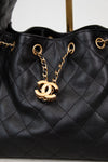 Black quilted handbag with gold chain and CC logo on a light gray background
