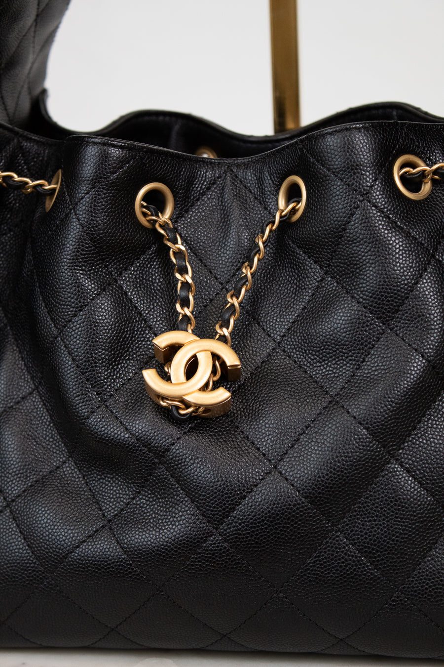 Black quilted handbag with gold chain and CC logo on a light gray background