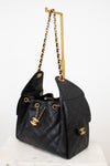 Black quilted handbag with gold chain strap on a white background