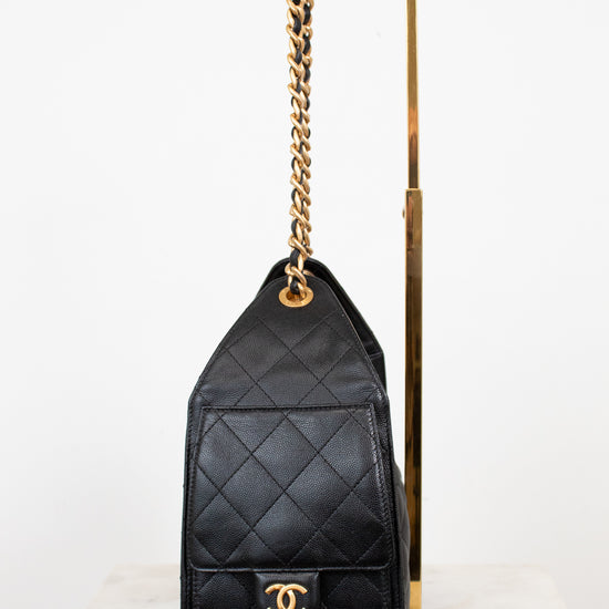 Black quilted handbag with gold chain and clasp on a white background