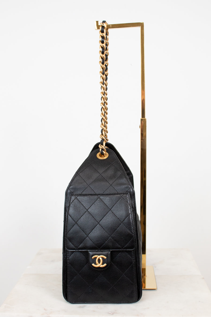 Black quilted handbag with gold chain and clasp on a white background