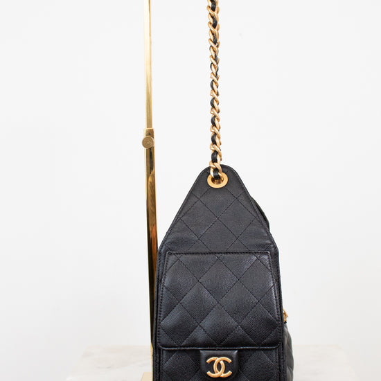 black quilted handbag with gold straps and gold Chanel logo sitting on a purse stand with white background