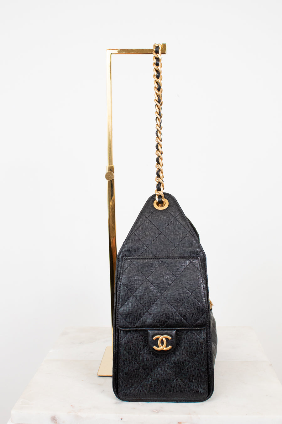 black quilted handbag with gold straps and gold Chanel logo sitting on a purse stand with white background