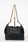 Black quilted handbag with gold strap details on a white background 
