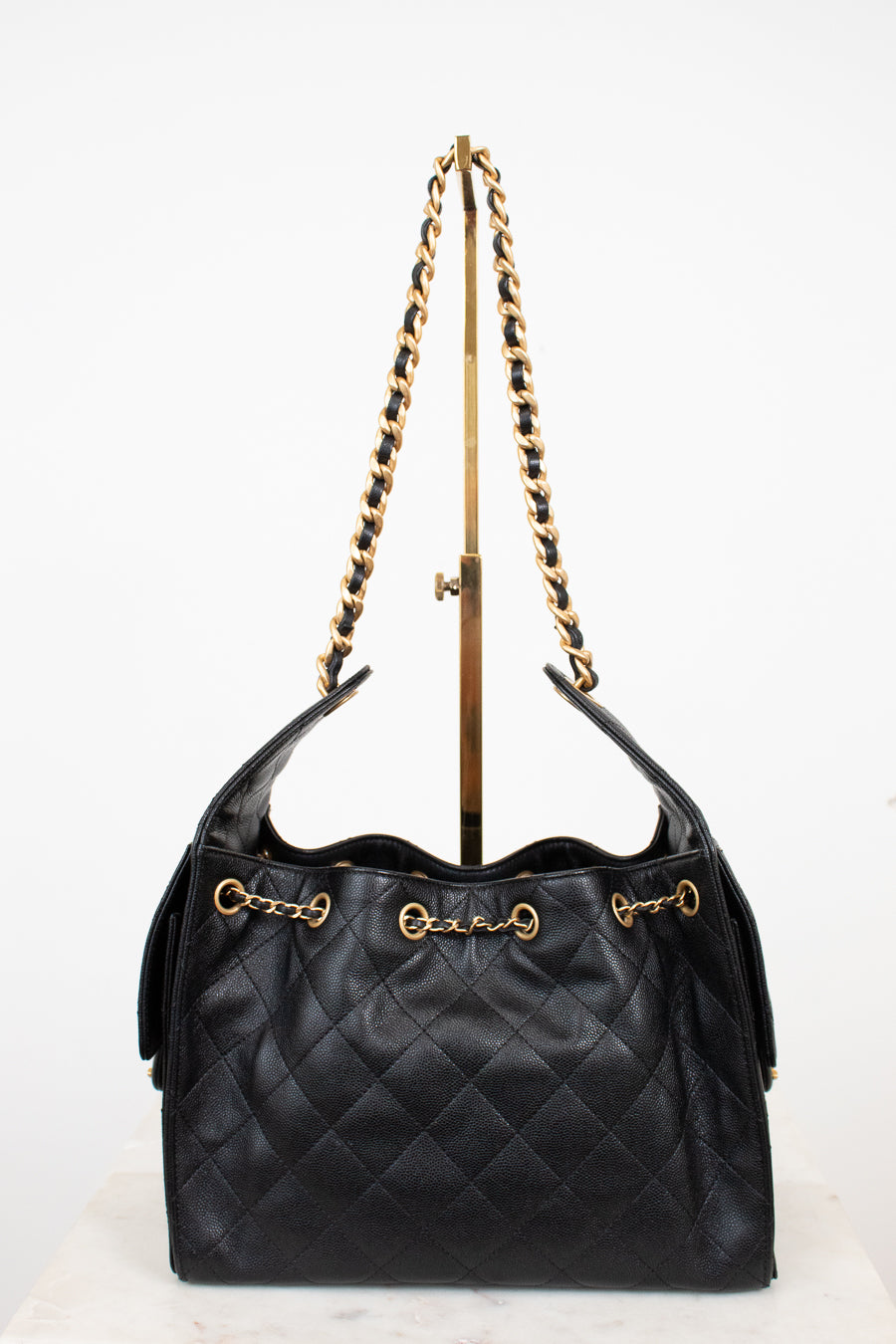 Black quilted handbag with gold strap details on a white background 