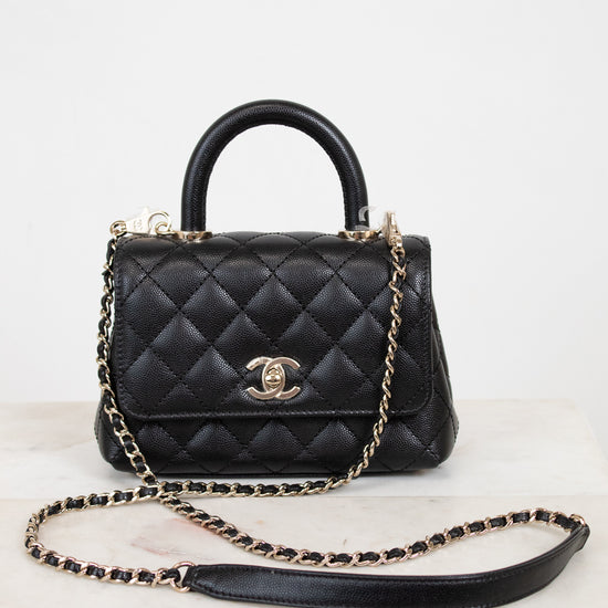Black quilted handbag with gold chain on a white background