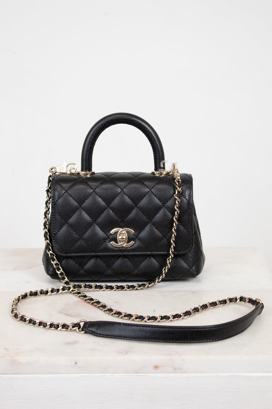 Black quilted handbag with gold chain on a white background