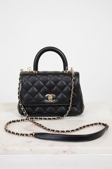 Black quilted handbag with gold chain on a white background