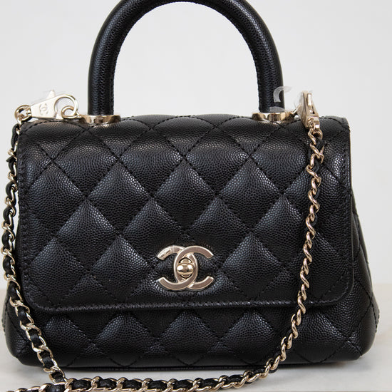 Black quilted handbag with gold chain and Chanel logo on a light background