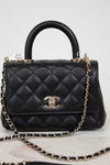 Black quilted handbag with gold chain and Chanel logo on a light background