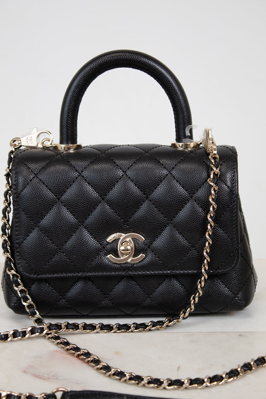 Black quilted handbag with gold chain and Chanel logo on a light background