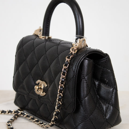 Black quilted handbag with gold chain and hardware on a light background
