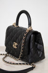 Black quilted handbag with gold chain and hardware on a light background