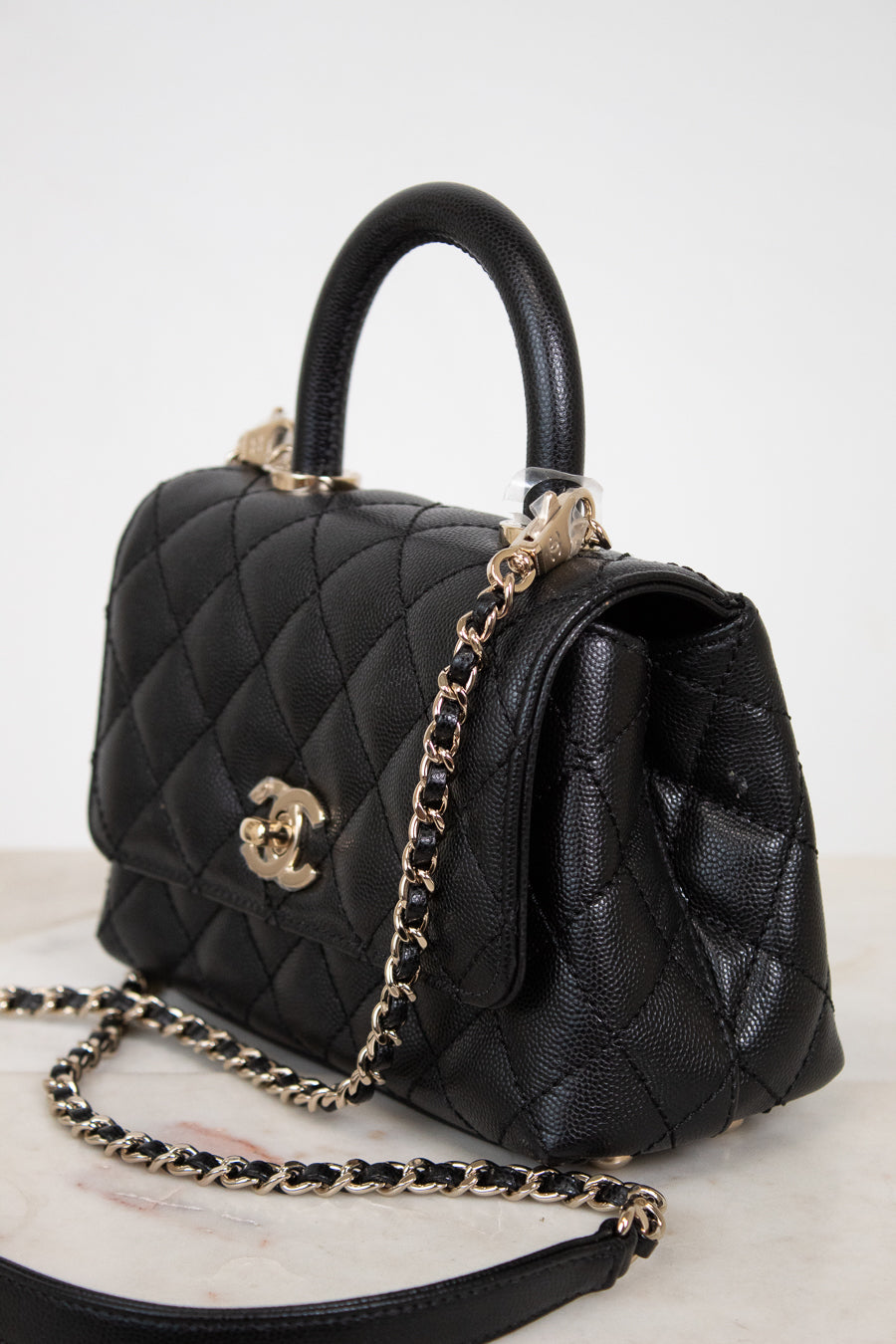 Black quilted handbag with gold chain and hardware on a light background