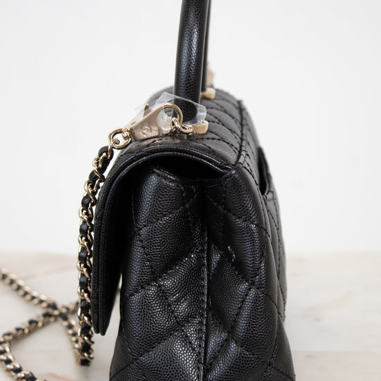 Black quilted handbag with a chain detail on a white background