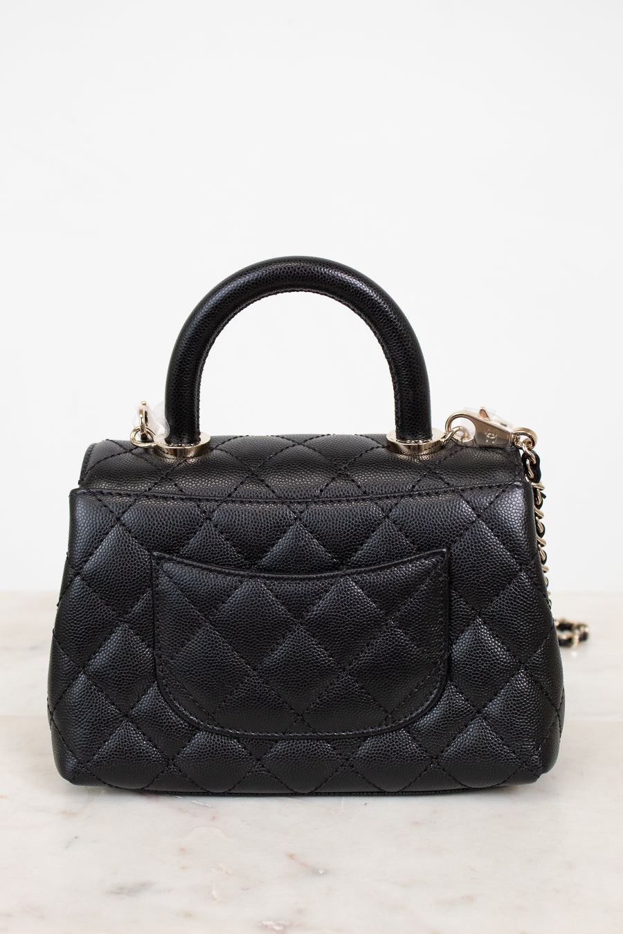Black leather handbag with gold hardware and chain detail on a white background