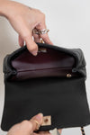 Person opening a black handbag with a visible brand logo on a neutral background