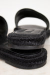 Close-up of black sandals with woven straps on a light background