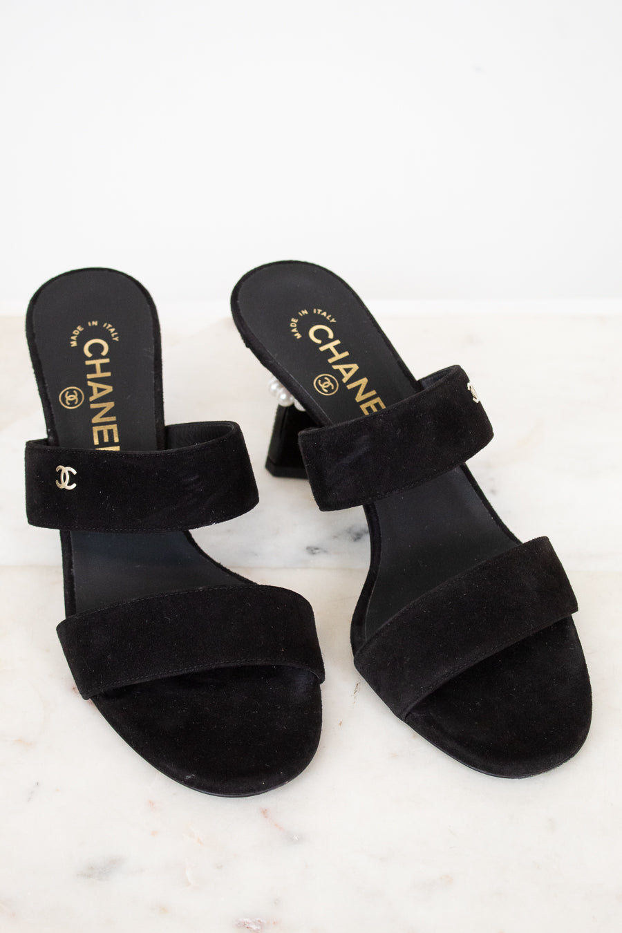 Black Chanel sandals on a white marble surface