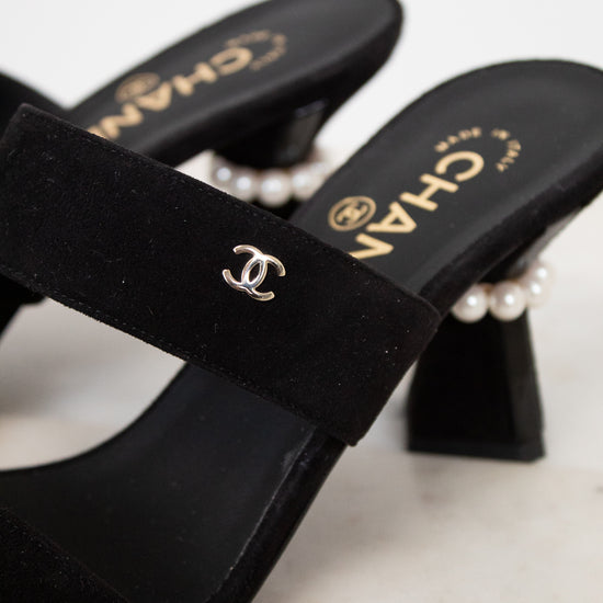 Black high-heeled shoes with pearl accents and Chanel logo on a light background