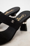 Black high-heeled shoes with pearl accents and Chanel logo on a light background