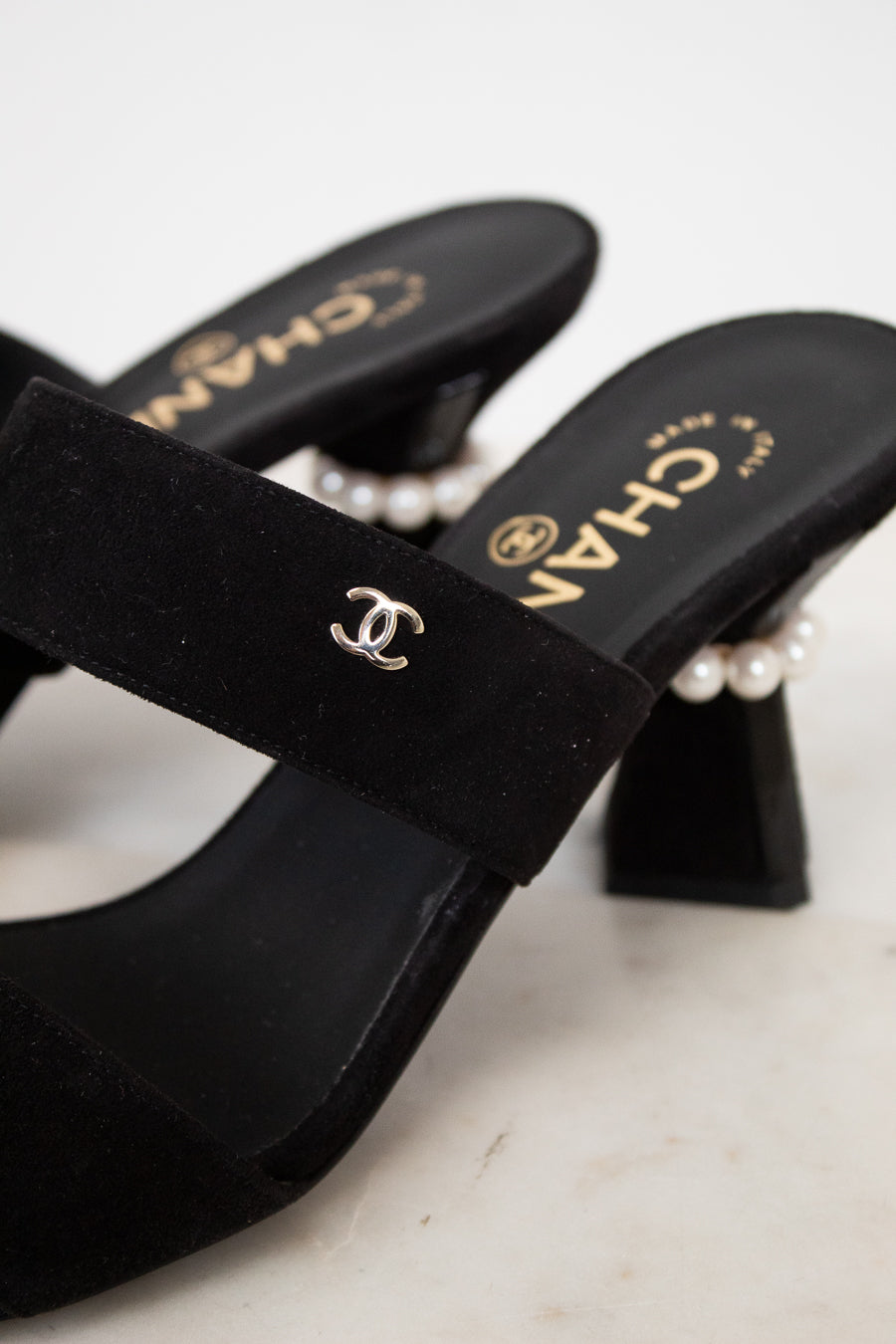 Black high-heeled shoes with pearl accents and Chanel logo on a light background