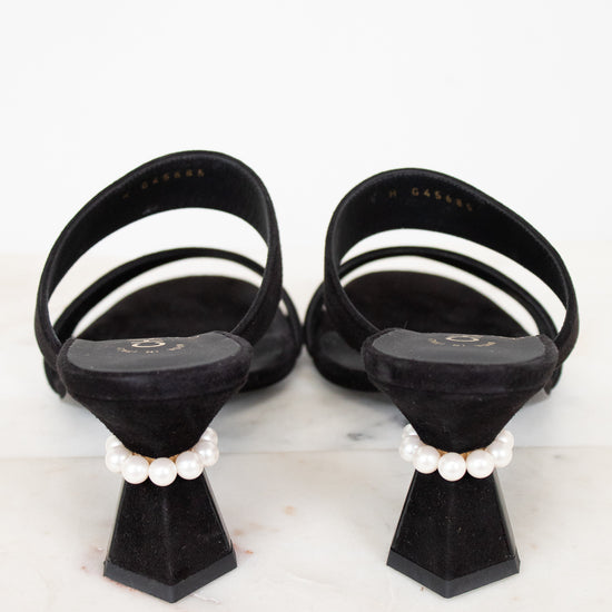 Black sandals with white straps and pearl embellishments on a light gray background
