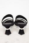 Black sandals with white straps and pearl embellishments on a light gray background