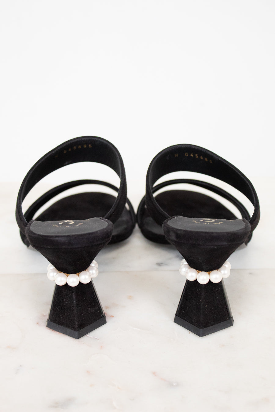 Black sandals with white straps and pearl embellishments on a light gray background