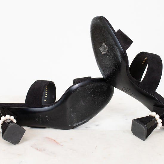 Black high-heeled shoes with pearl accents on a white surface