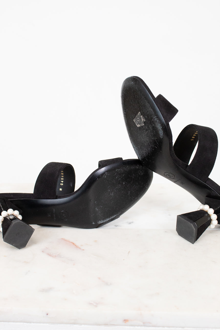 Black high-heeled shoes with pearl accents on a white surface