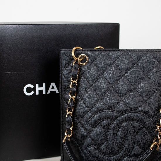 A black quilted Chanel shoulder bag with gold-tone chain strap and interlocking CC logo, displayed next to its black Chanel box on a light surface.