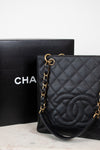 A black quilted Chanel shoulder bag with gold-tone chain strap and interlocking CC logo, displayed next to its black Chanel box on a light surface.